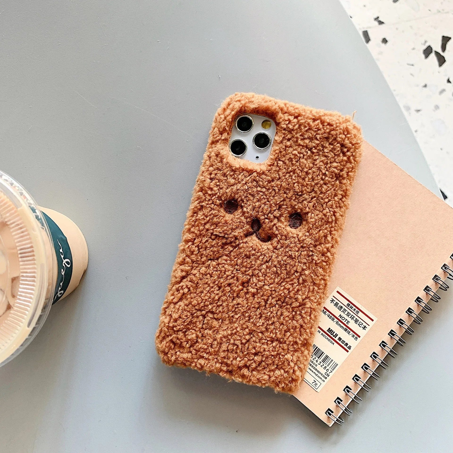 Brown soft TPU iPhone case featuring a raised plush bear face with embroidered details.
