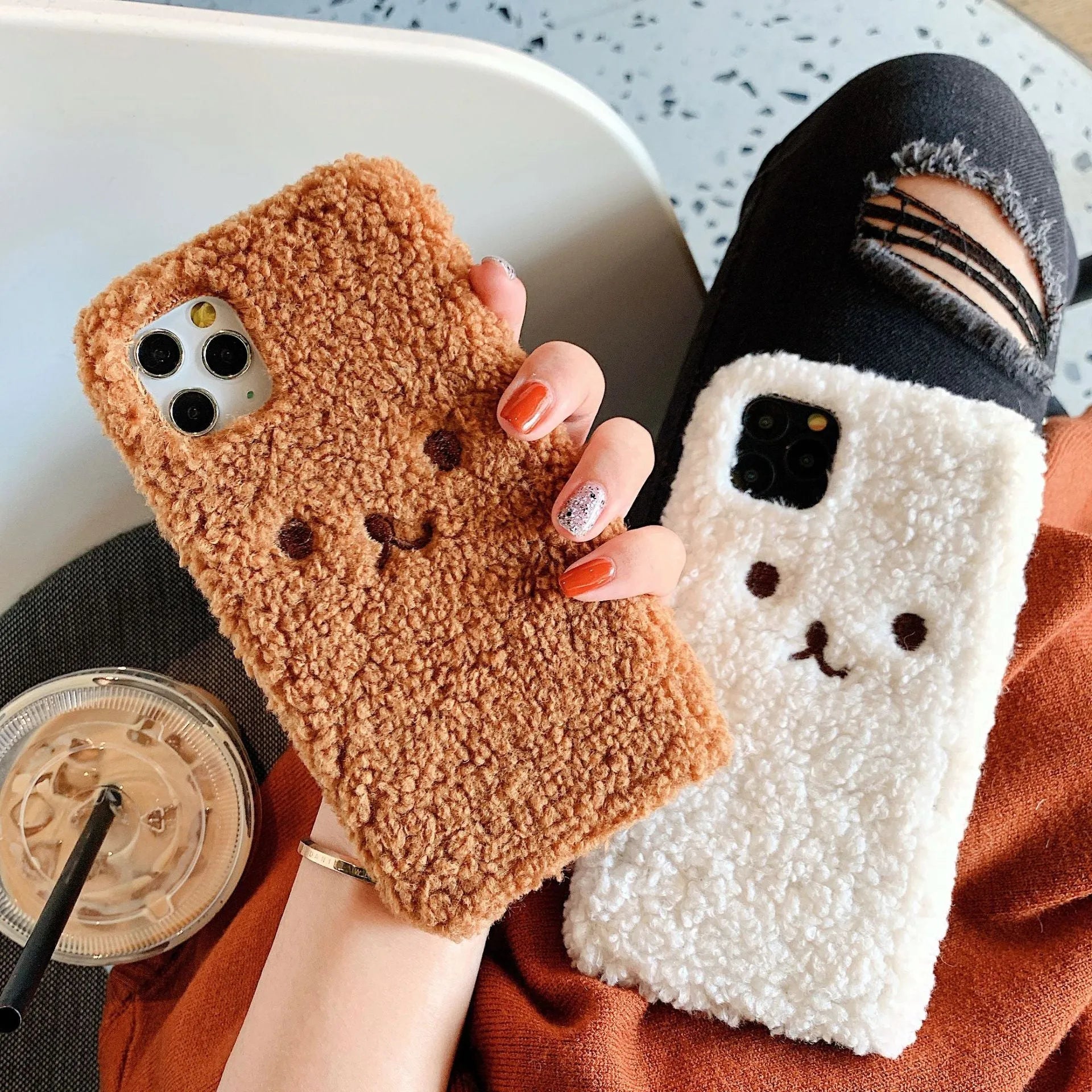 Brown embroidered plush bear face on a clear TPU phone case for iPhone, showing precise button and camera cutouts.