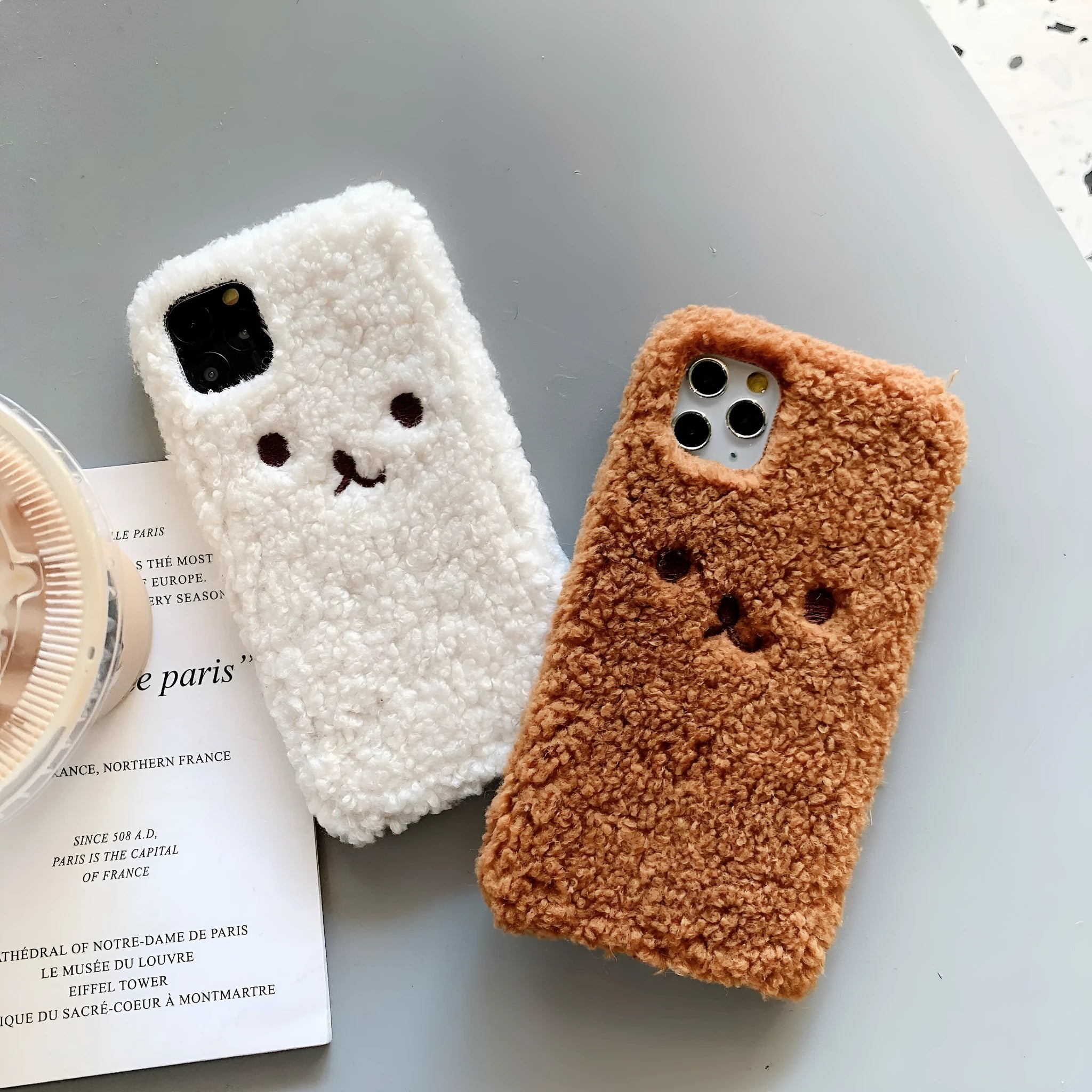 Brown embroidered plush bear face on a clear TPU phone case for iPhone, showing precise button and camera cutouts.