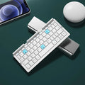 Silver white folding Bluetooth keyboard open with phone in stand next to closed black grey version