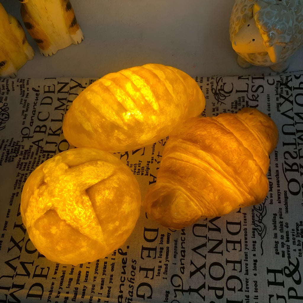 Battery-powered croissant-shaped LED night light with plastic shade on a table.