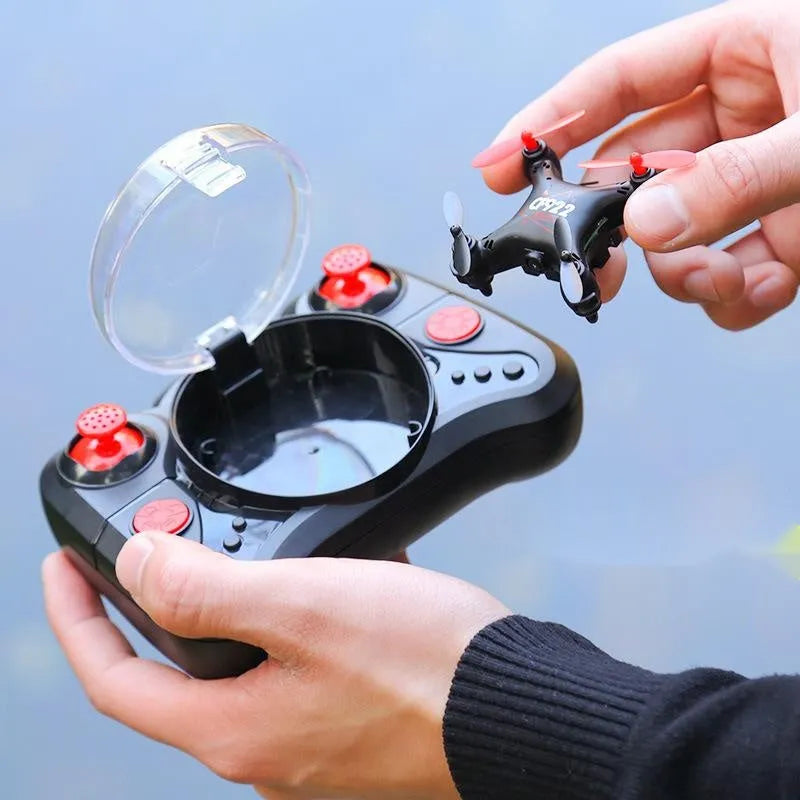 Compact black remote control aircraft with four rotors and a handheld remote control on a table.