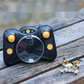 Compact black remote control aircraft with four rotors and a handheld remote control on a table.