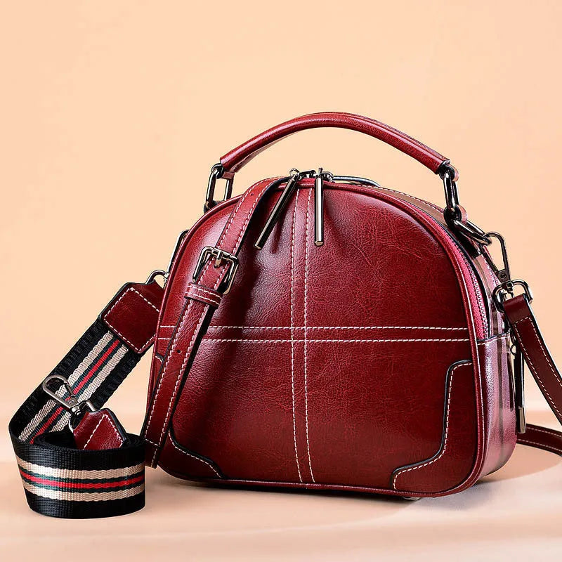 A round leather handbag with soft handles and a zipper top, shown in a wine red colour.