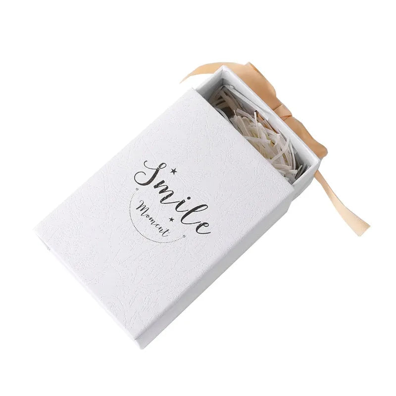 Small cardboard gift box with handbag and raffia in blue, pink, red, or white, showing bronzing detail.