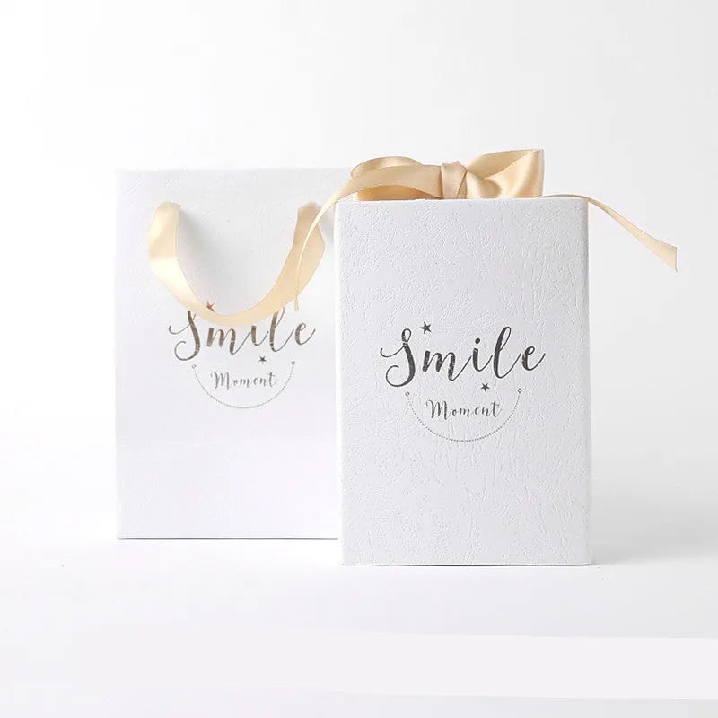 Small cardboard gift box with handbag and raffia in blue, pink, red, or white, showing bronzing detail.