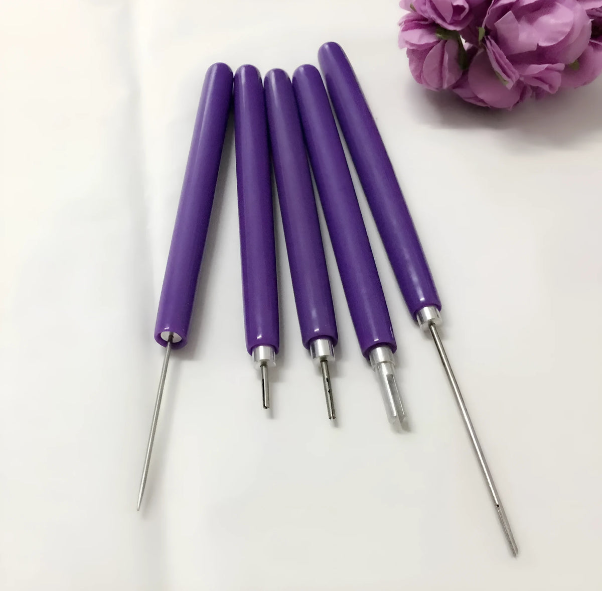 Five purple quilling pens with slotted tips and a stylus laid out on a surface