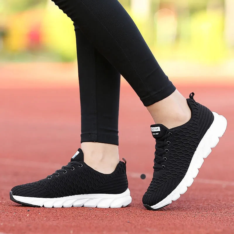 Women's running shoes in black, pink, and white colours showing fly weaving upper and rubber outsole.