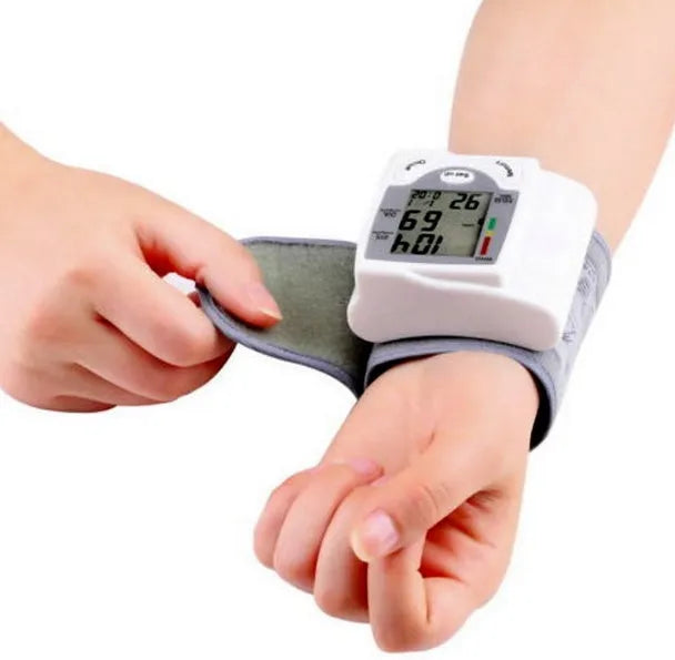 Grey portable wrist blood pressure monitor with digital display on a wrist.