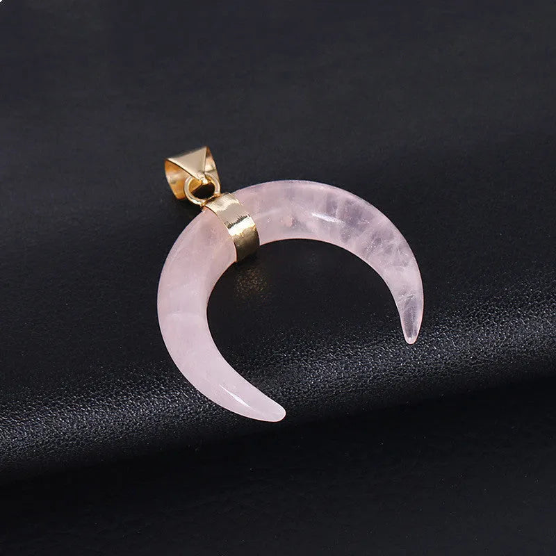 Close-up of a moon-shaped pink natural stone pendant on a metallic chain necklace.