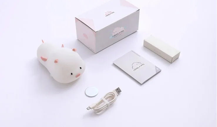 Blue rechargeable pig-shaped silicone night light with soft glow on a bedside table.