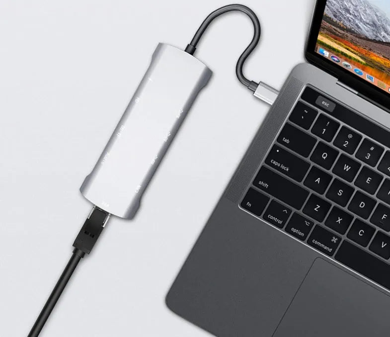 Grey aluminium USB-C docking station with HDMI, VGA, USB 3.0, and PD charge ports on a wooden desk.