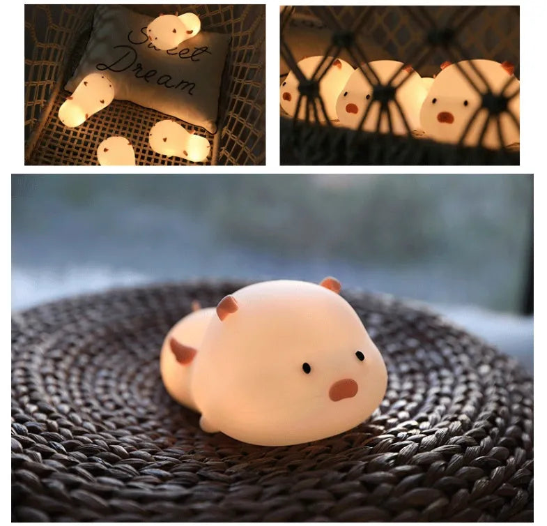 Blue rechargeable pig-shaped silicone night light with soft glow on a bedside table.