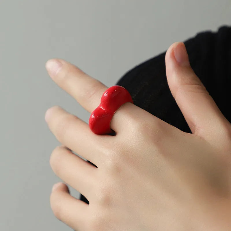 Heart-shaped zinc alloy ring with three-dimensional enamel colour in black, pink, purple, or red on a finger.