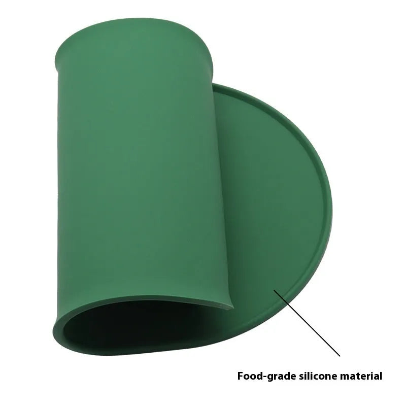 Green silicone cat feeding mat with raised edge under a ceramic food and water bowl on a wooden floor.