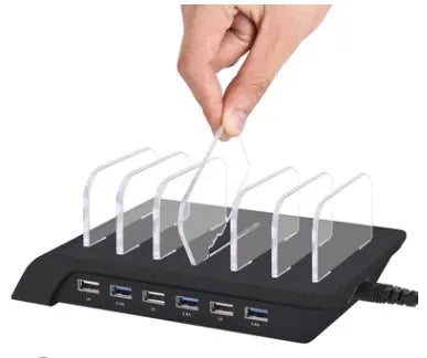 Six-port USB mobile phone charging stand in silver with multiple phones and tablets inserted, on a wooden desk