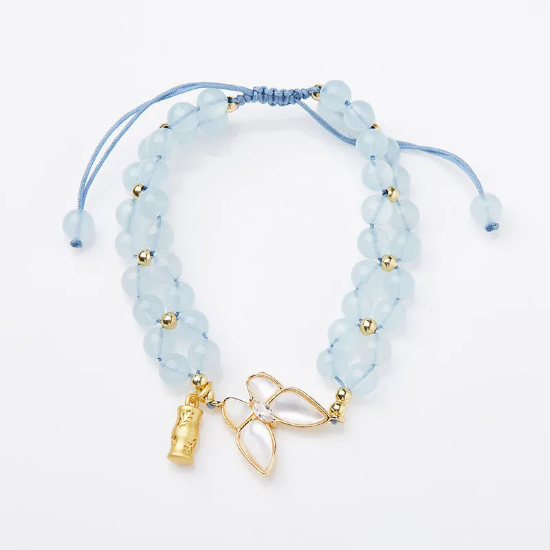 Close-up of a women's woven bracelet with a butterfly motif and a central aquamarine gemstone bead.