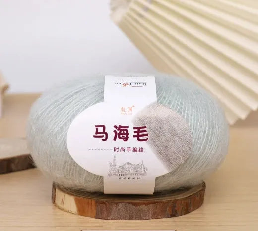 A ball of mohair yarn in a selected colour next to a hand-woven scarf example, showcasing the DIY kit.