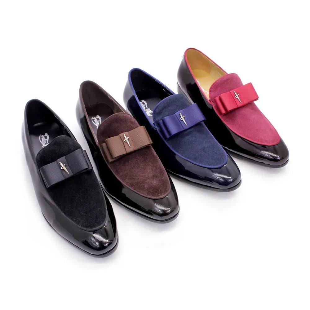 Men's black tassel loafers with glossy patent leather upper and matte leather toe holder on a wooden floor.