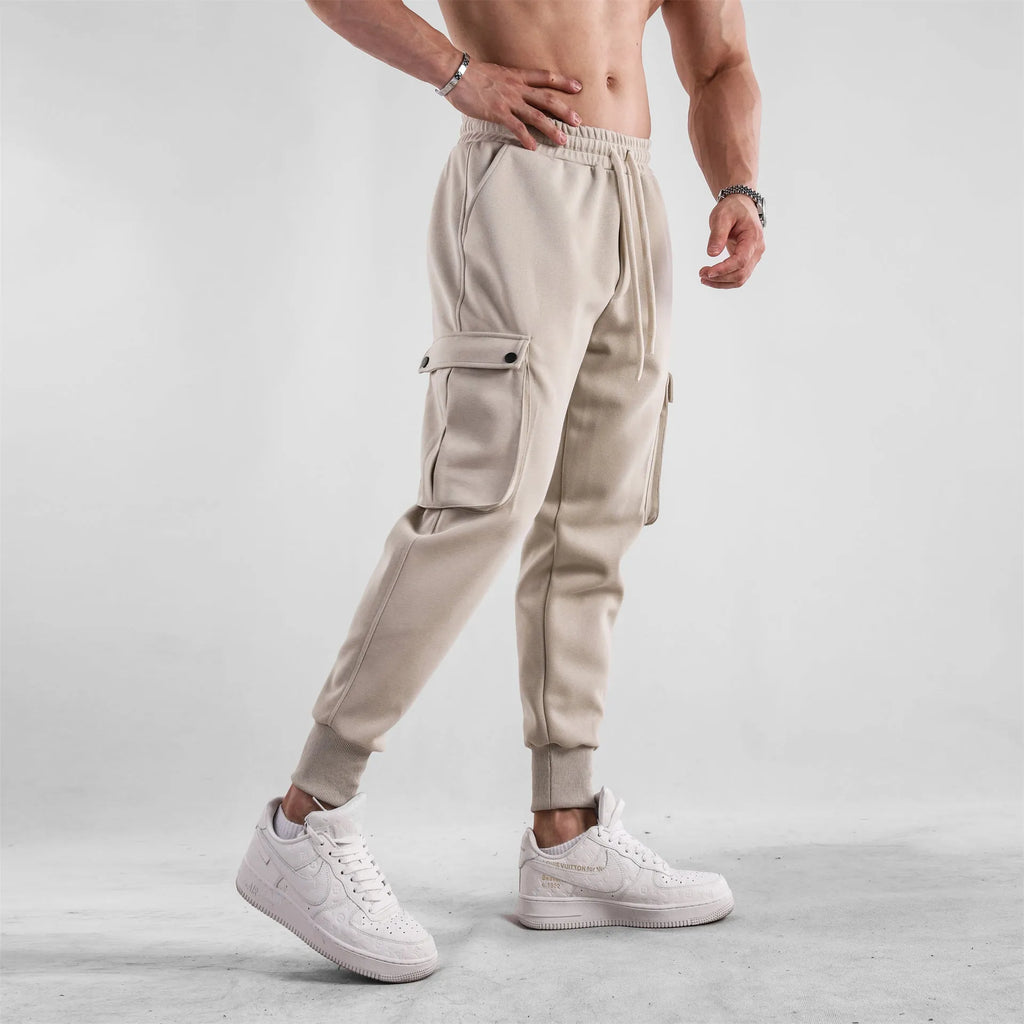 Men's loose-fit beige cotton trousers with tied ankle cuffs and multiple pockets on the legs.