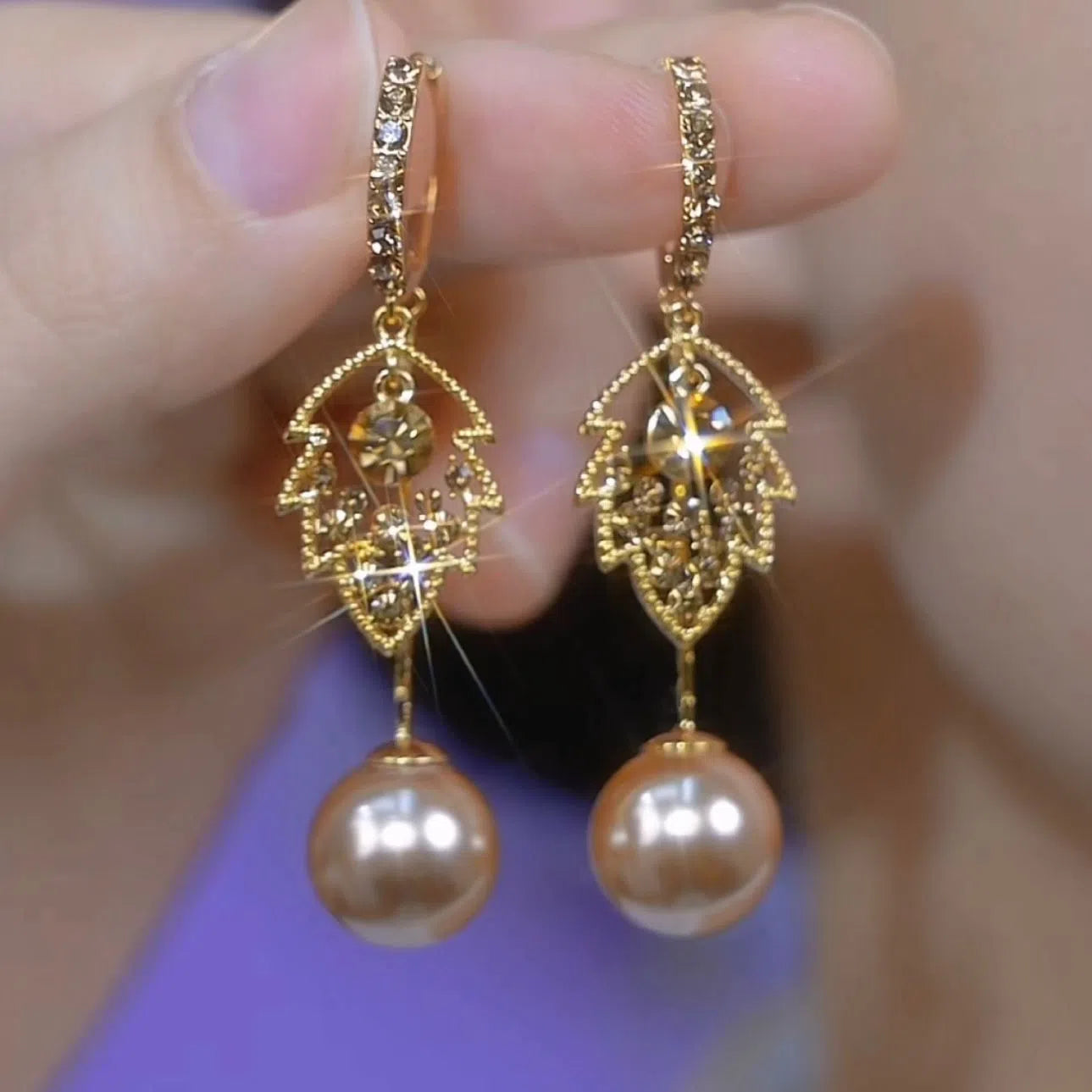 Coffee-coloured metal leaf earrings with full diamond-cut surface and pearl accents, old money style, side view on white background