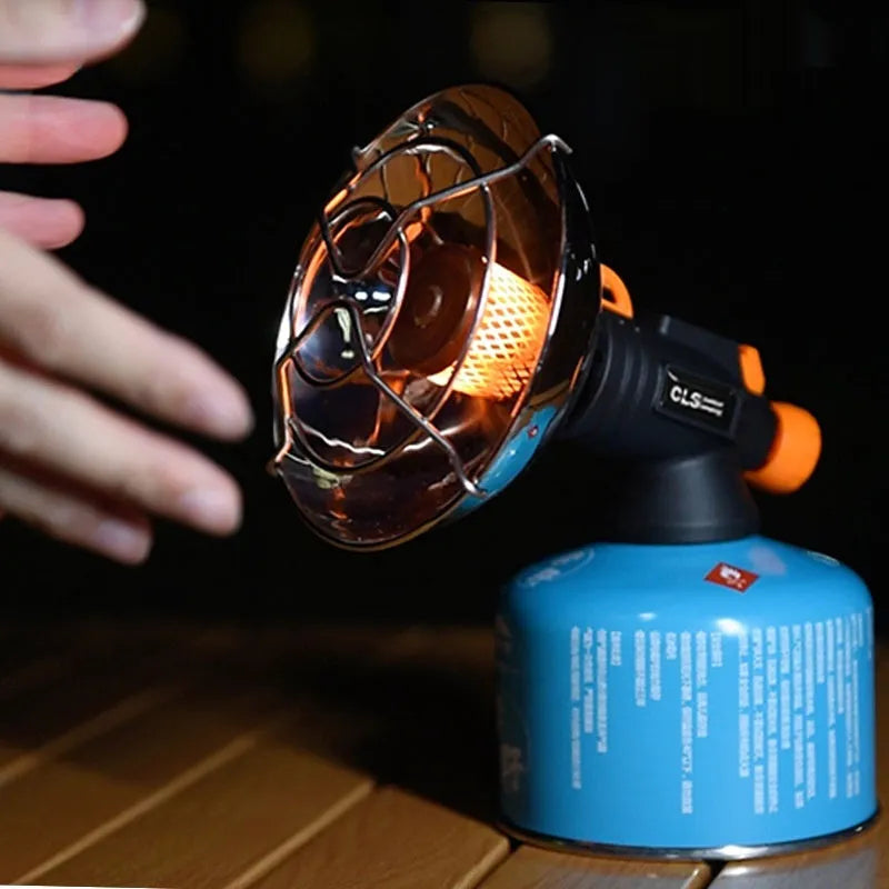 Black and orange portable camping stove with automatic ignition on a rocky outdoor surface.