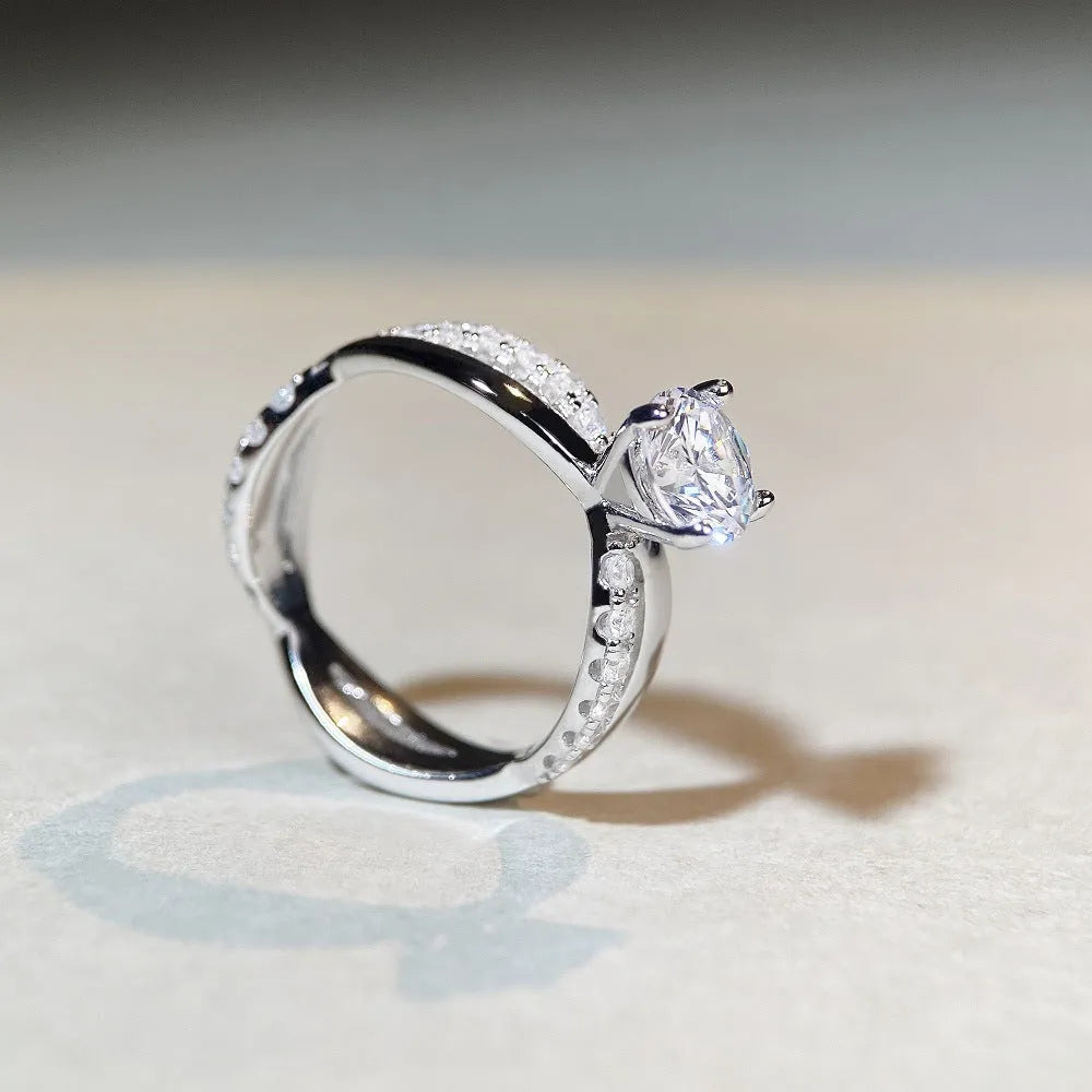 Silver ring with a 1 karat moissanite stone in a twisted four-claw setting, showing geometric lines and a cross design.