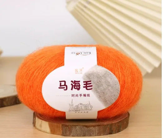 A ball of mohair yarn in a selected colour next to a hand-woven scarf example, showcasing the DIY kit.