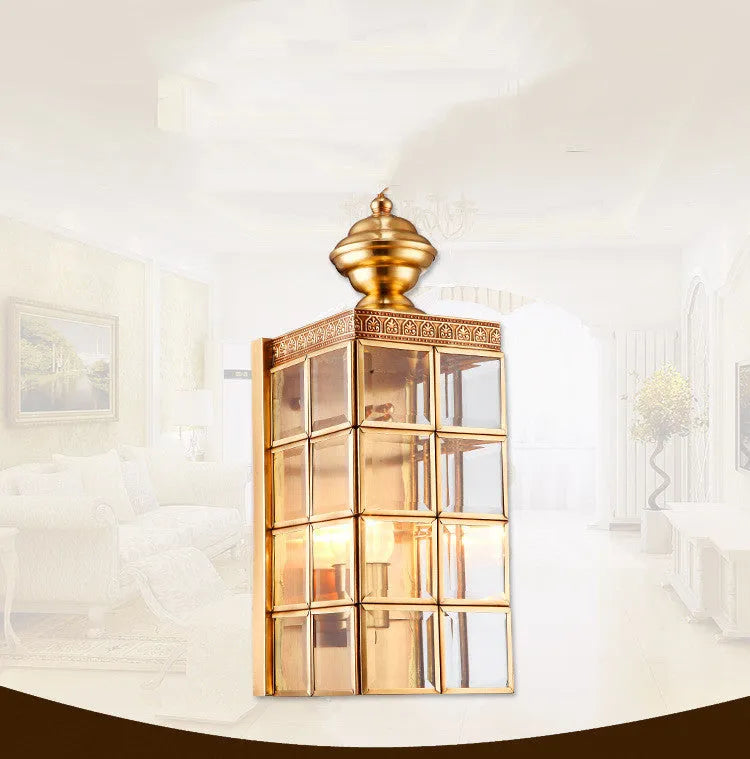 Full copper wall lamp with glass shade and gold finish on a brick balcony wall