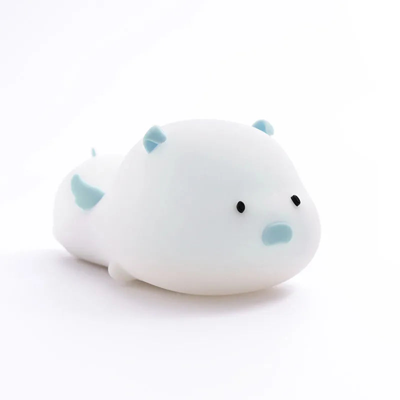 Blue rechargeable pig-shaped silicone night light with soft glow on a bedside table.