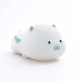 Blue rechargeable pig-shaped silicone night light with soft glow on a bedside table.