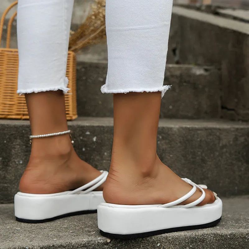 Thick-soled flip-flop slippers in a herringbone pattern, shown in various colours on a sandy background.