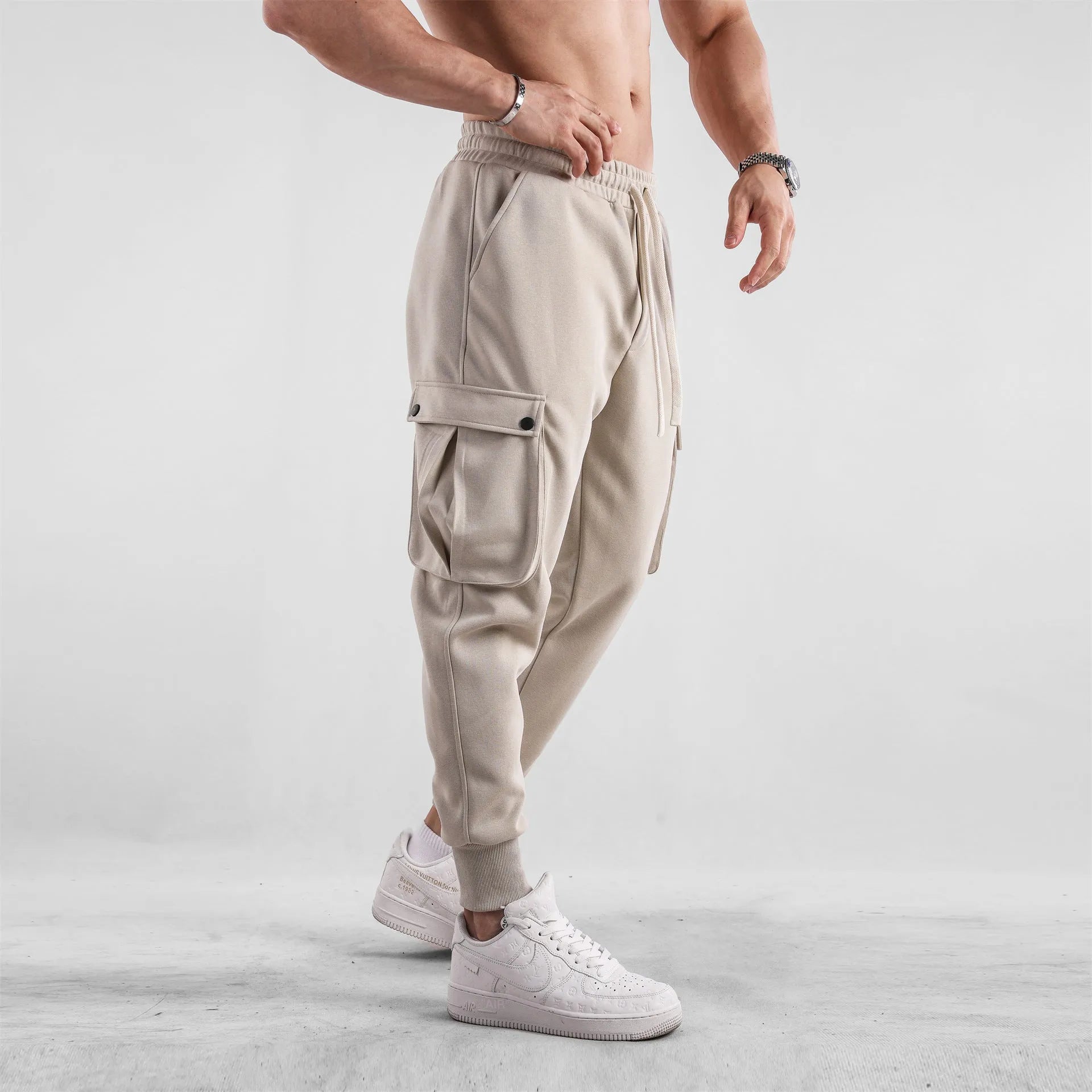 Men's loose-fit beige cotton trousers with tied ankle cuffs and multiple pockets on the legs.