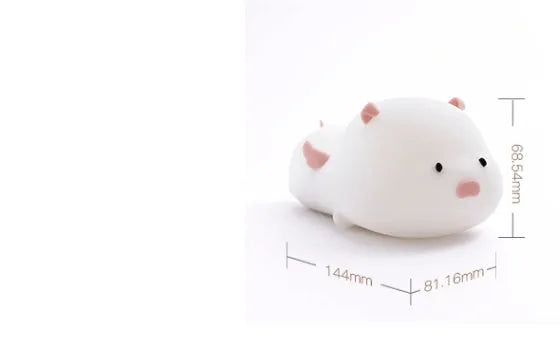 Blue rechargeable pig-shaped silicone night light with soft glow on a bedside table.