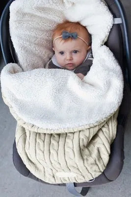 Envelope-style baby stroller sleeping bag in beige colour with thick filling, shown next to a pram.