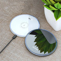 Black aluminium 15W Qi wireless fast charger for phones on a wooden desk.