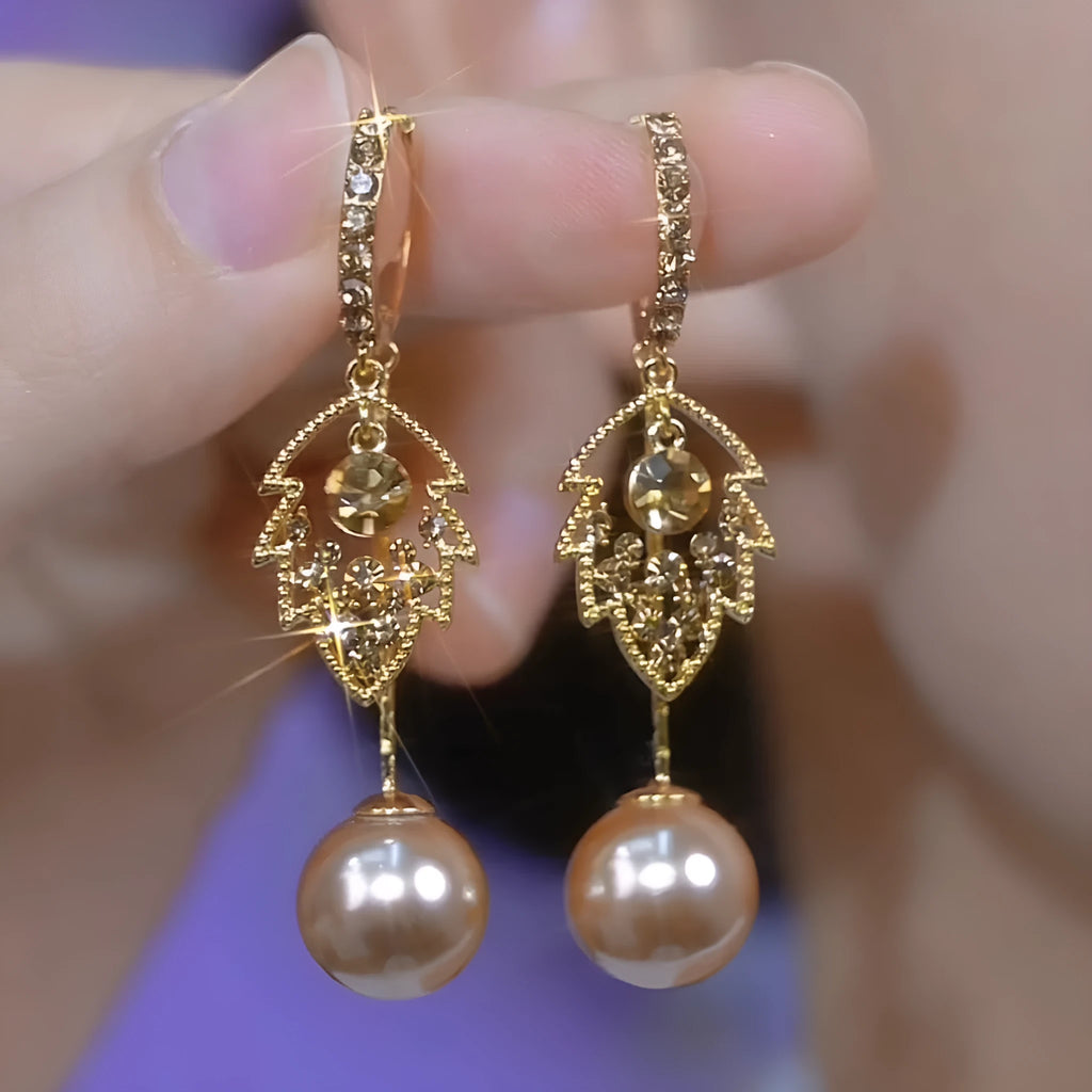 Coffee-coloured metal leaf earrings with full diamond-cut surface and pearl accents, old money style, side view on white background