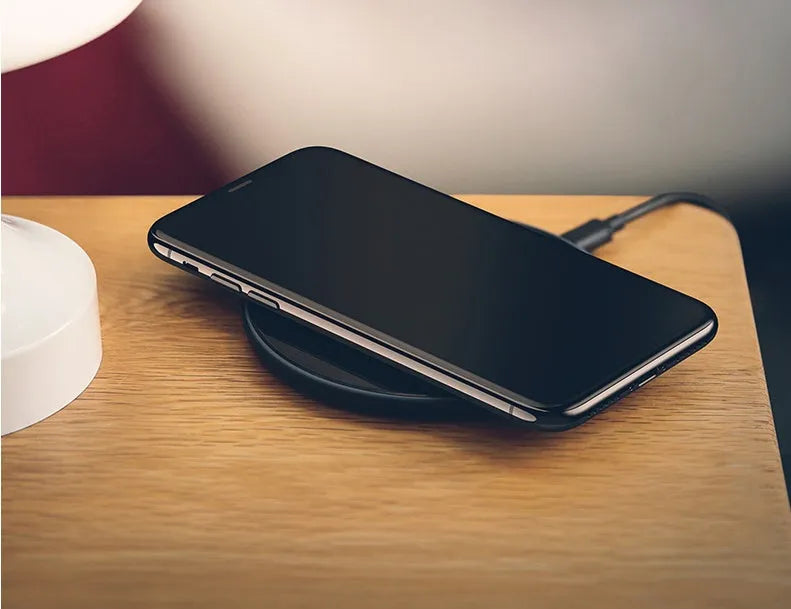 A black or white glass disc wireless charger on a table, showing its sleek design.