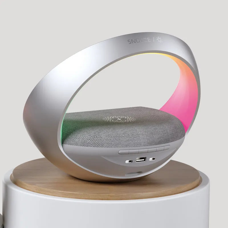 Beige multifunctional wireless charging Bluetooth speaker with clock and adjustable LED mood lighting on a wooden table.