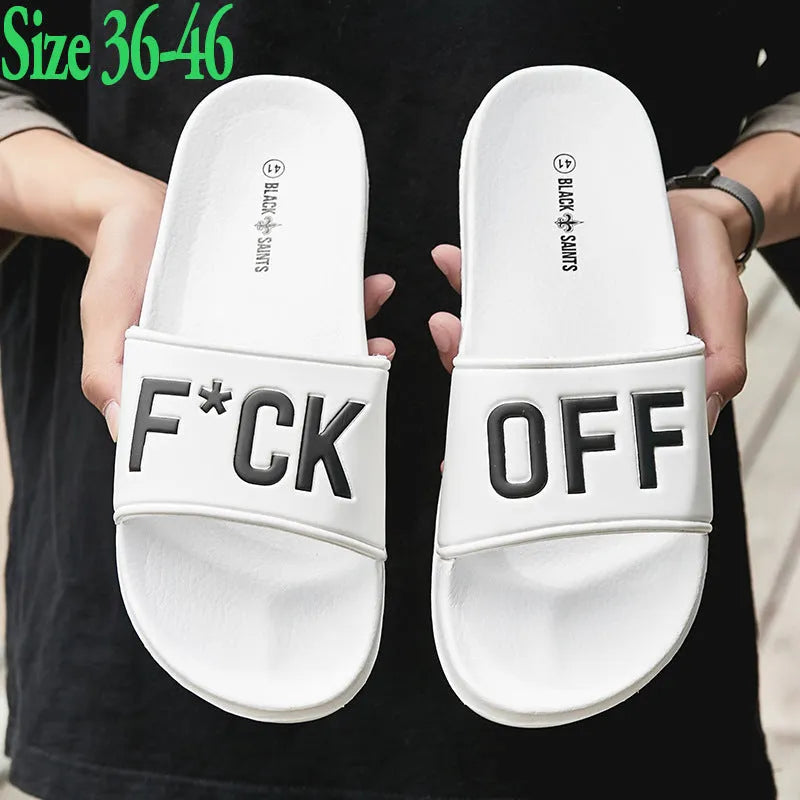 Large black and white open-toe men's slippers with rubber soles, shown on a wooden floor.