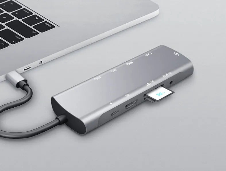 Grey aluminium USB-C docking station with HDMI, VGA, USB 3.0, and PD charge ports on a wooden desk.