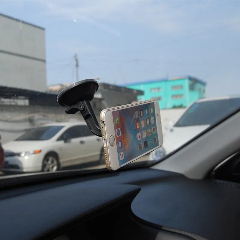 Black magnetic car phone holder mounted on a car dashboard, showing a smartphone attached.
