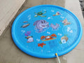 Blue children's water spray mat with marine animals laid on grass, connected to a garden hose.