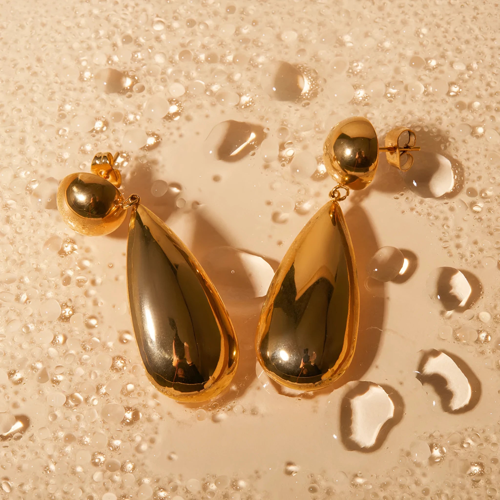 A pair of gold-coloured stainless steel pendant earrings with a geometric water drop hemisphere shape.