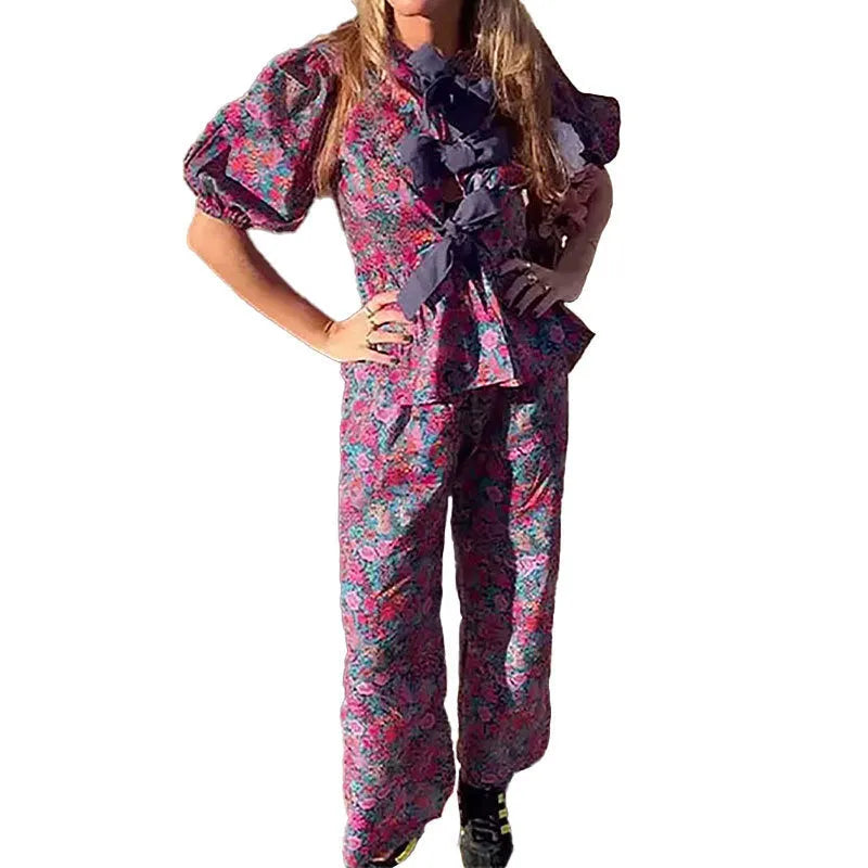 Women's floral printed trousers suit with a tie-neck blouse featuring puff sleeves and matching trousers.