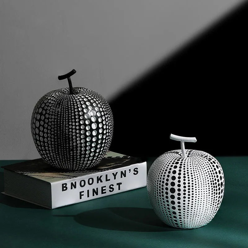 A black resin apple figurine and a white resin pear figurine on a wooden surface.
