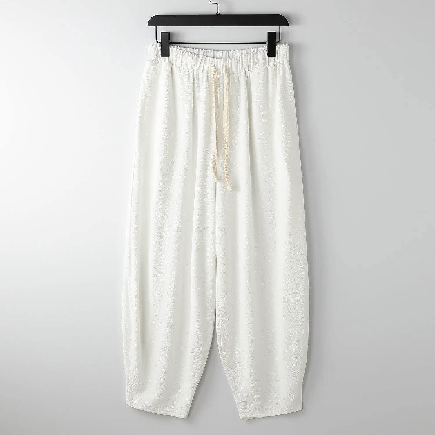 Man wearing loose-fitting, light-coloured linen harem pants with tapered legs and an elasticated ankle tie.