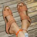 Pair of beige Roman style slippers with a fish mouth toe holder and slope heel on a rubber sole.