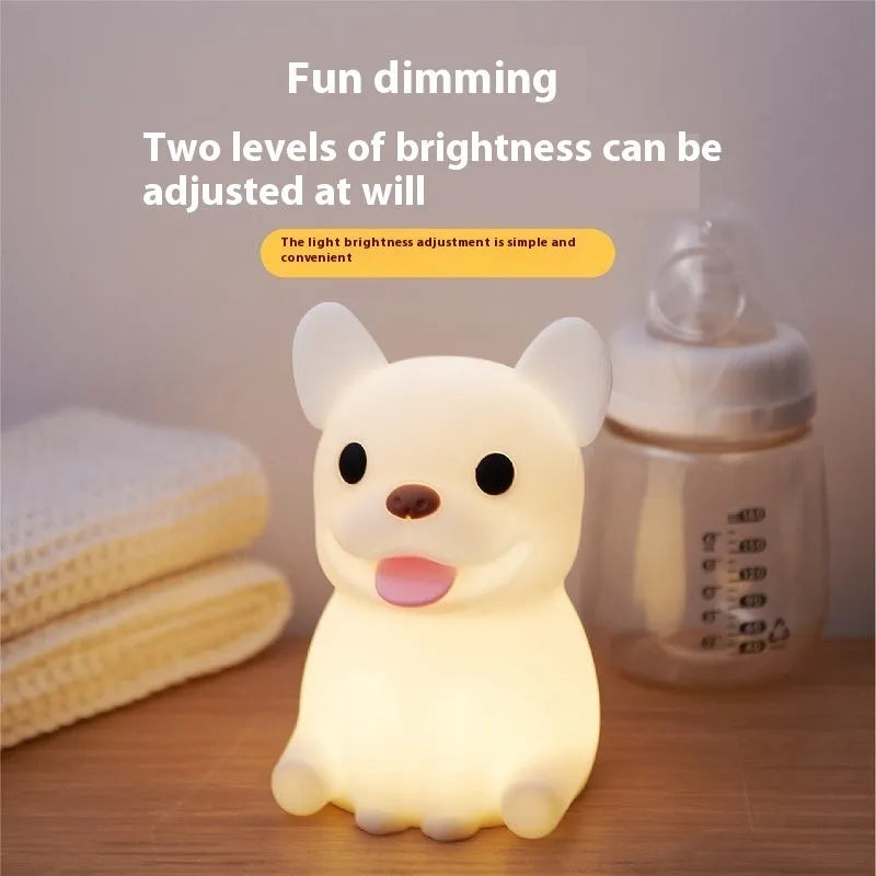 Soft silicone animal or cartoon-themed USB night light with dimming function on a bedside table.