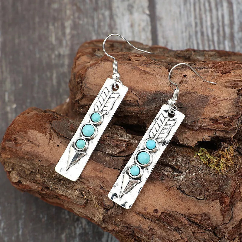 Silver geometric drop earrings with turquoise inlaid accents on a plain background